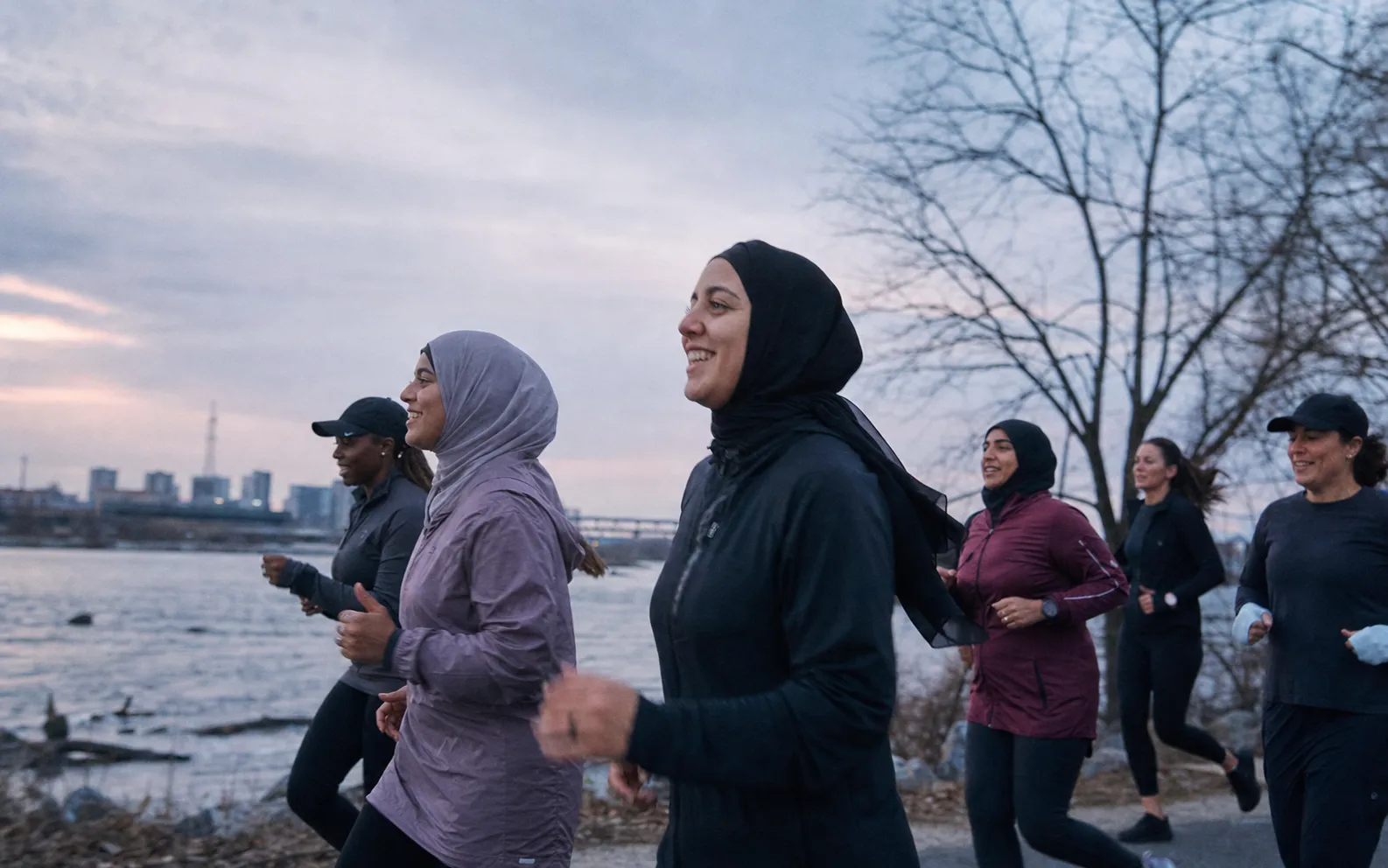 A group of women running together beside the river in cool morning light